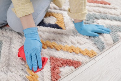 Photo of Woman in rubber gloves cleaning carpet with rag indoors, closeup