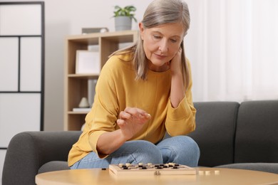 Photo of Thoughtful senior woman playing checkers at home