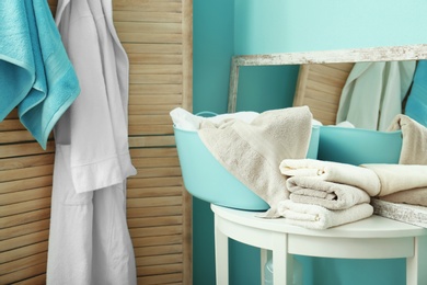 Stack of clean towels and laundry basket on table in bathroom