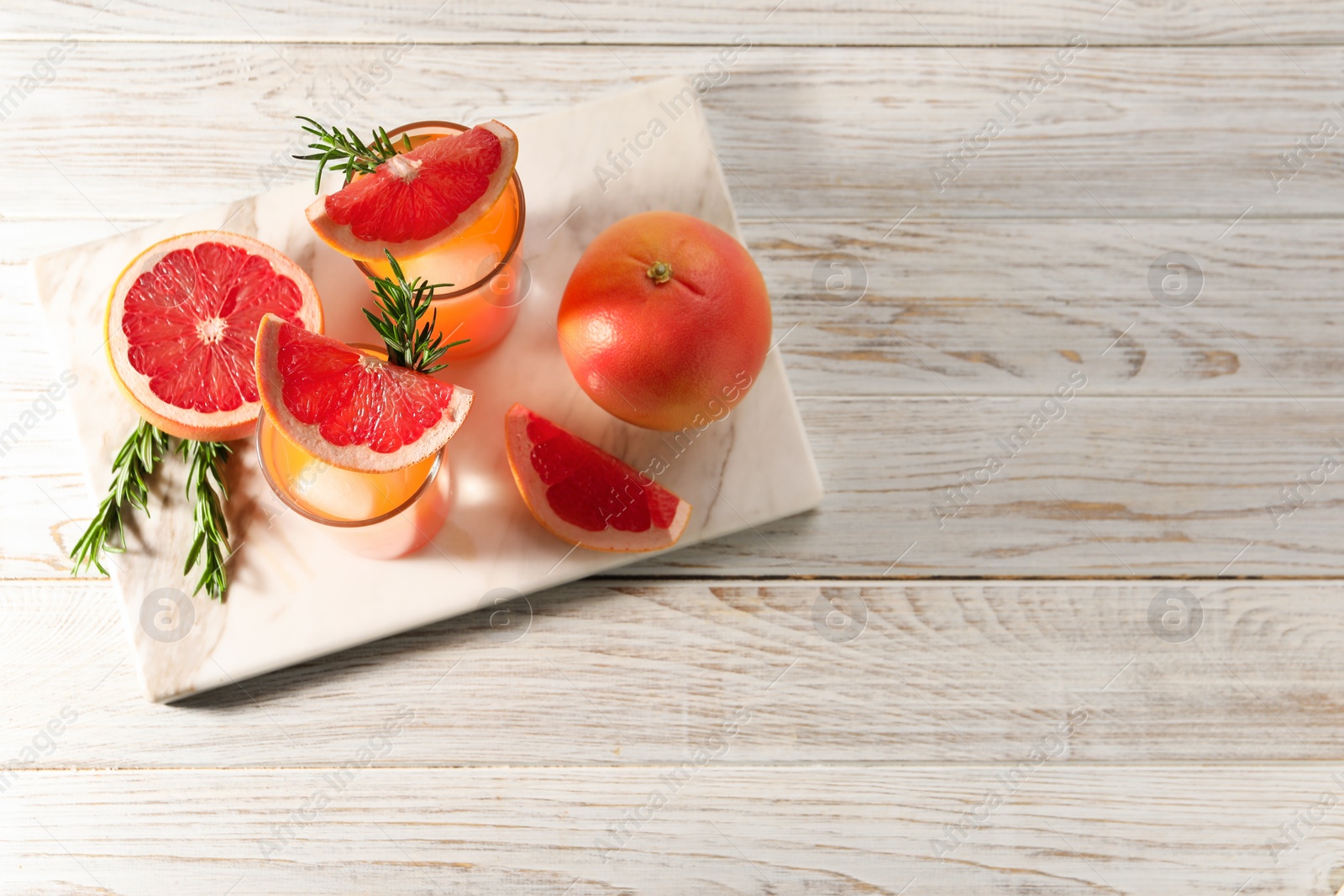 Photo of Tasty grapefruit drink with ice in glasses, rosemary and fresh fruits on light wooden table, top view. Space for text