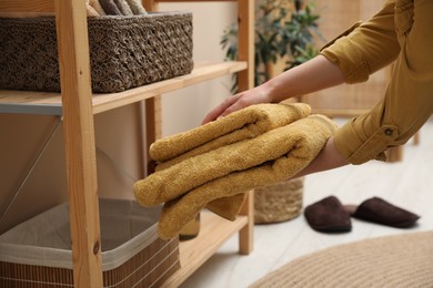 Photo of Woman putting towels into storage basket indoors, closeup