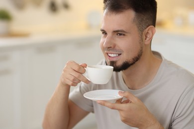 Smiling man drinking coffee at breakfast on blurred background