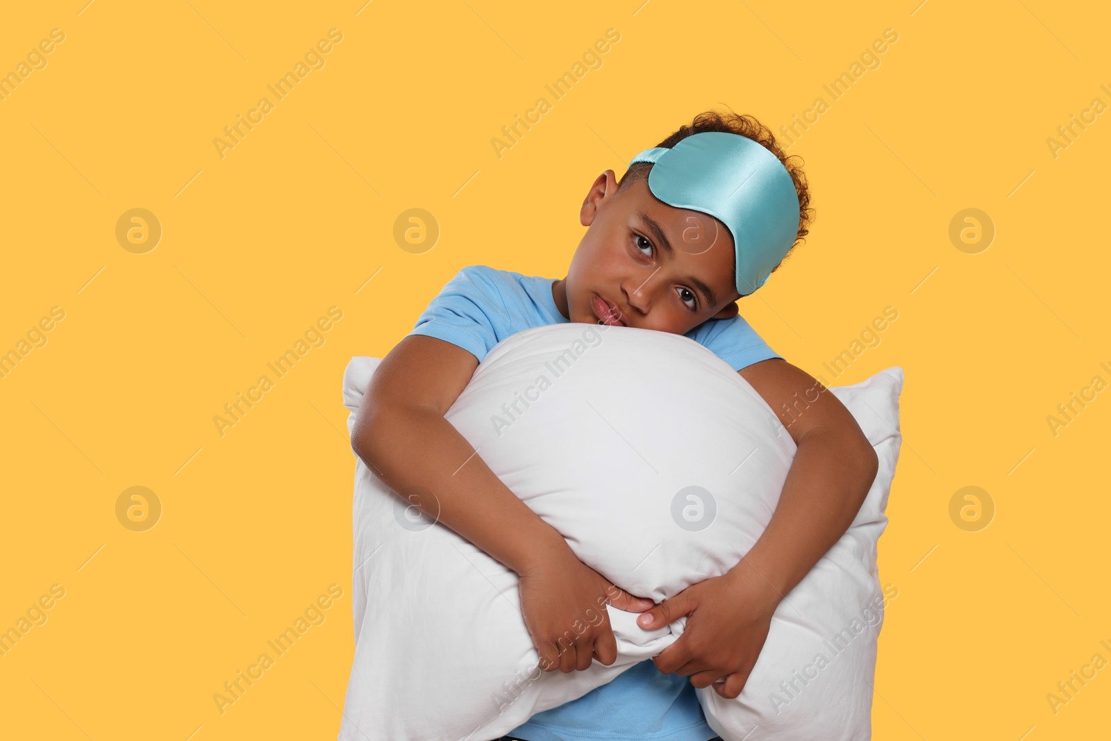Photo of Boy with pillow and sleep mask on yellow background. Insomnia problem