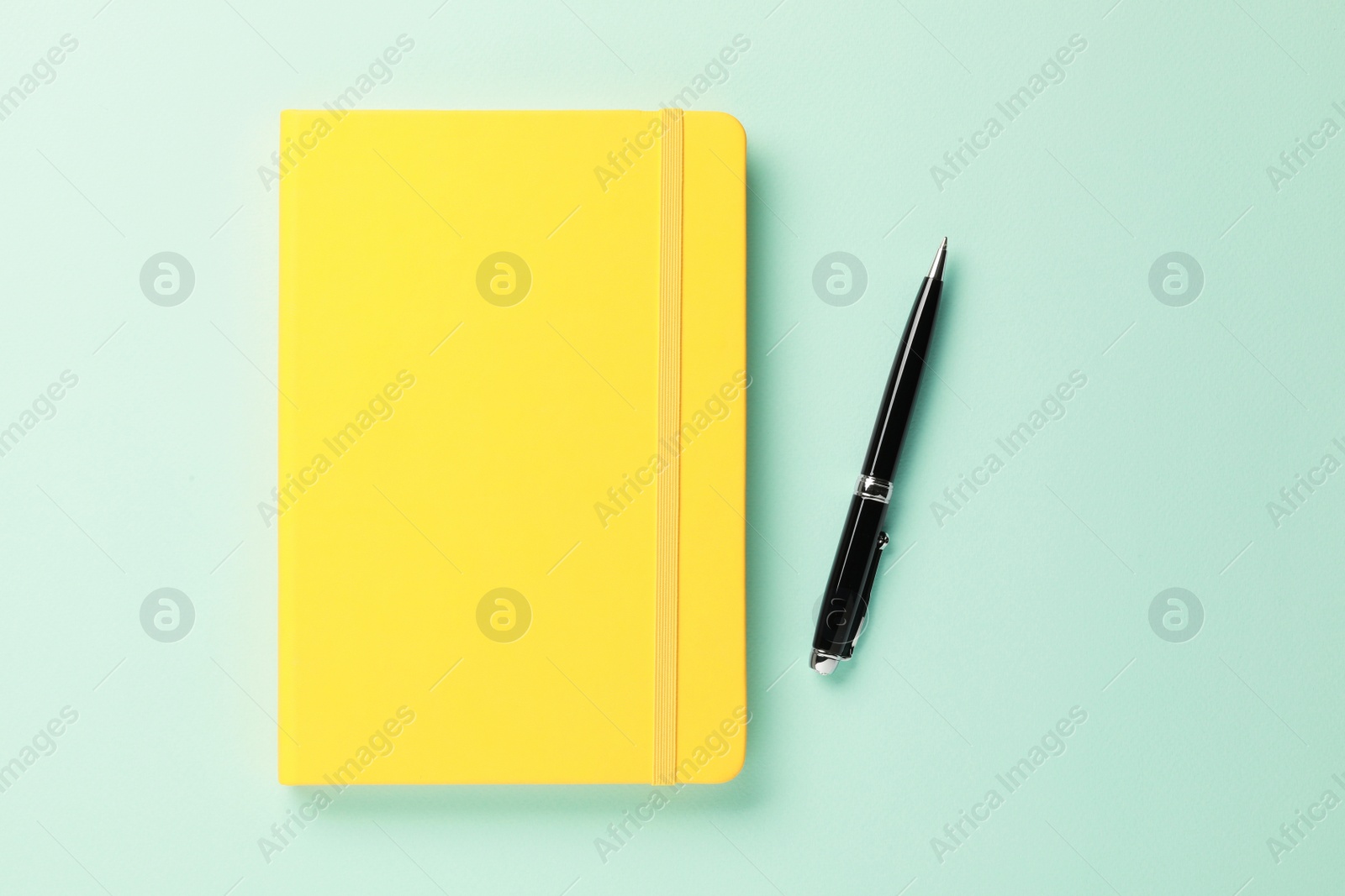 Photo of Yellow notebook and pen on turquoise background, flat lay