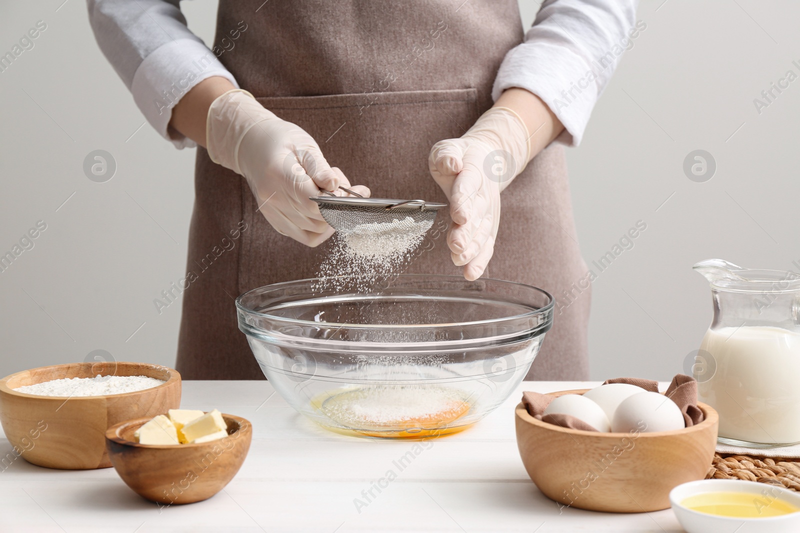 Photo of Woman preparing batter for crepes at white wooden table, closeup