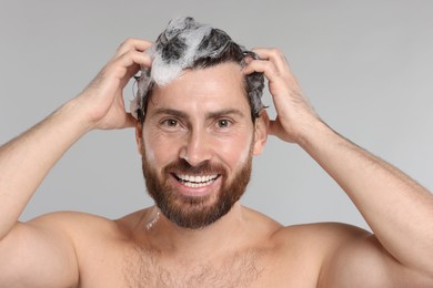 Photo of Happy man washing his hair with shampoo on grey background, closeup