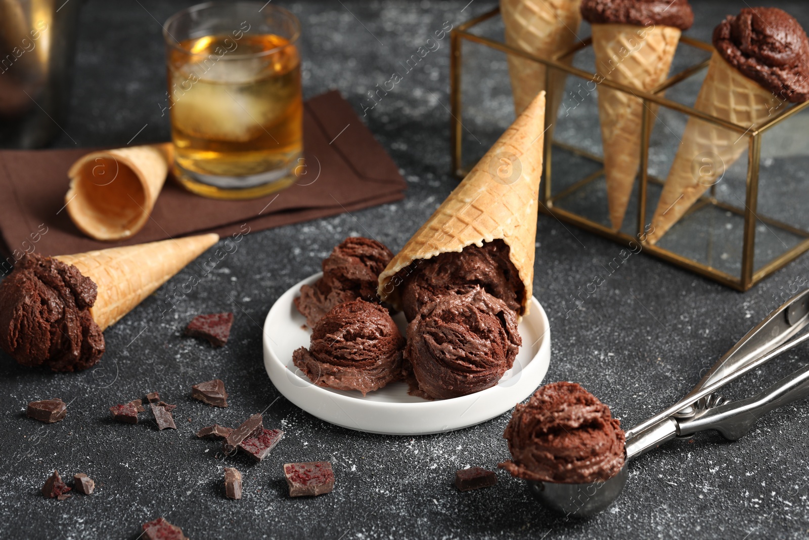 Photo of Tasty ice cream scoops, chocolate crumbs and waffle cones on dark textured table, closeup