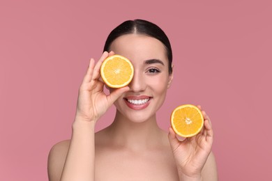 Beautiful young woman with pieces of orange on pink background