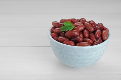 Photo of Bowl of canned kidney beans with parsley on white wooden table, closeup. Space for text