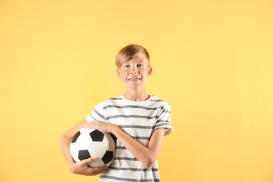 Portrait of young boy holding soccer ball on color background