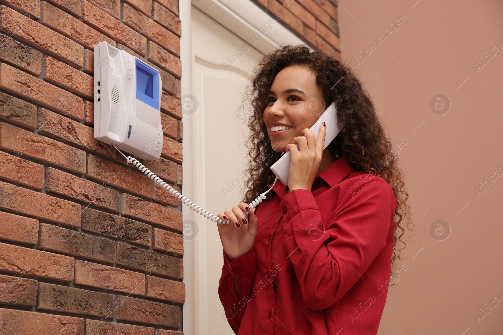 Photo of Young African-American woman answering intercom call indoors