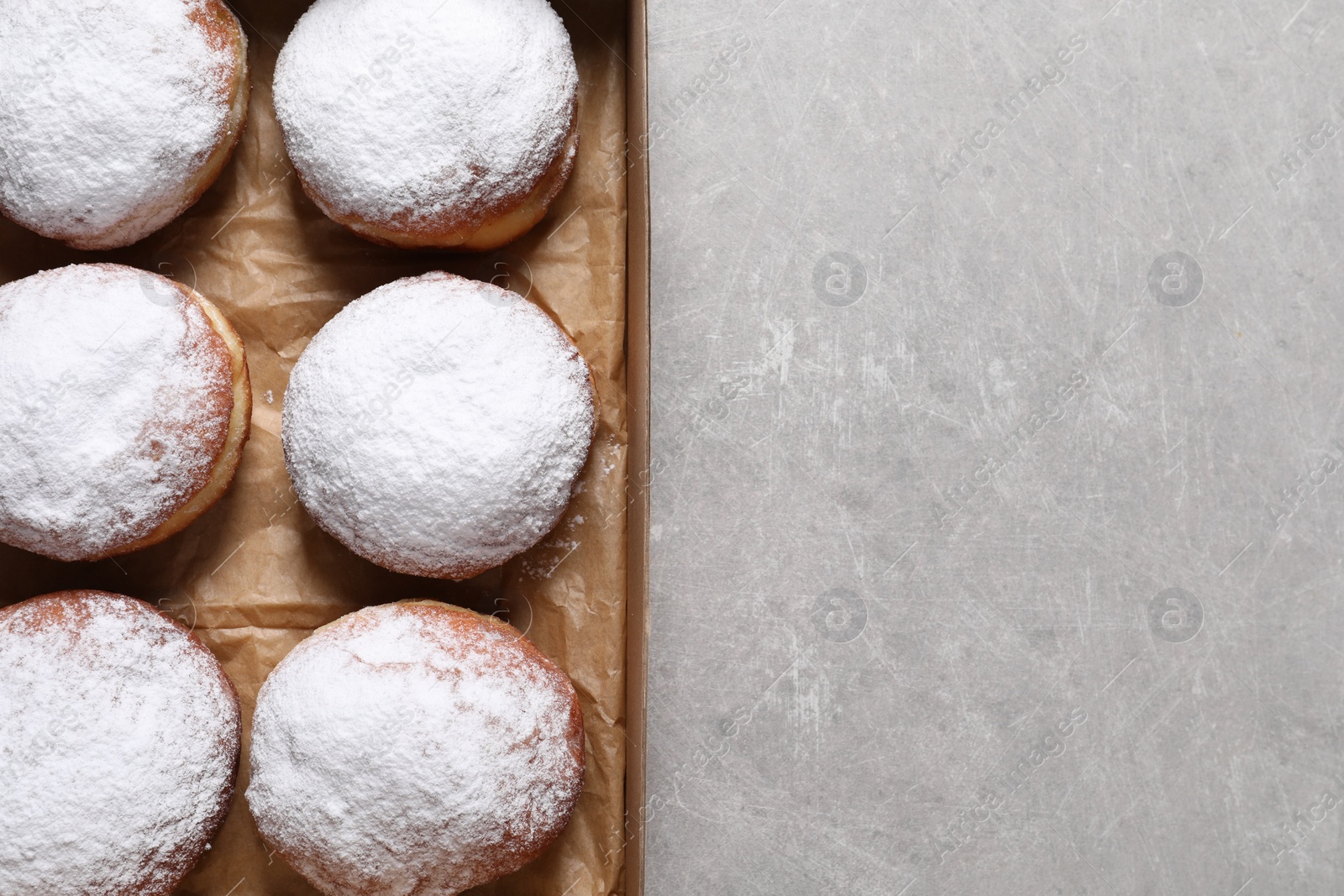 Photo of Delicious buns with powdered sugar in box on light grey table, top view. Space for text