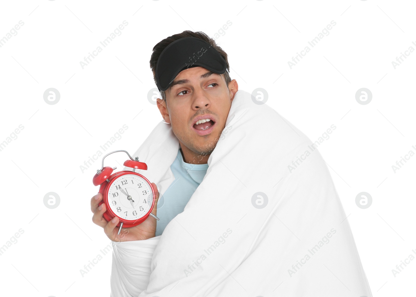 Photo of Man in sleeping mask wrapped with blanket holding alarm clock on white background