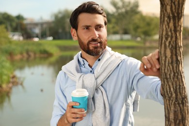 Portrait of handsome bearded man with coffee near lake, space for text
