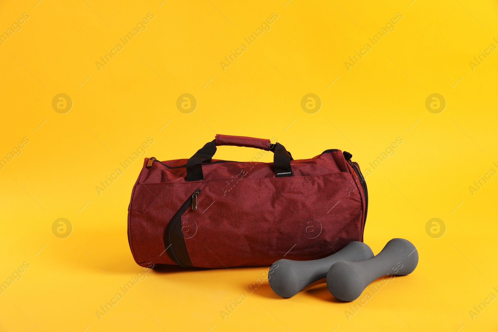Photo of Sports bag and dumbbells on yellow background