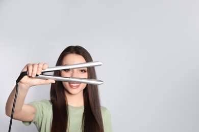 Photo of Happy woman with hair iron on grey background. Space for text