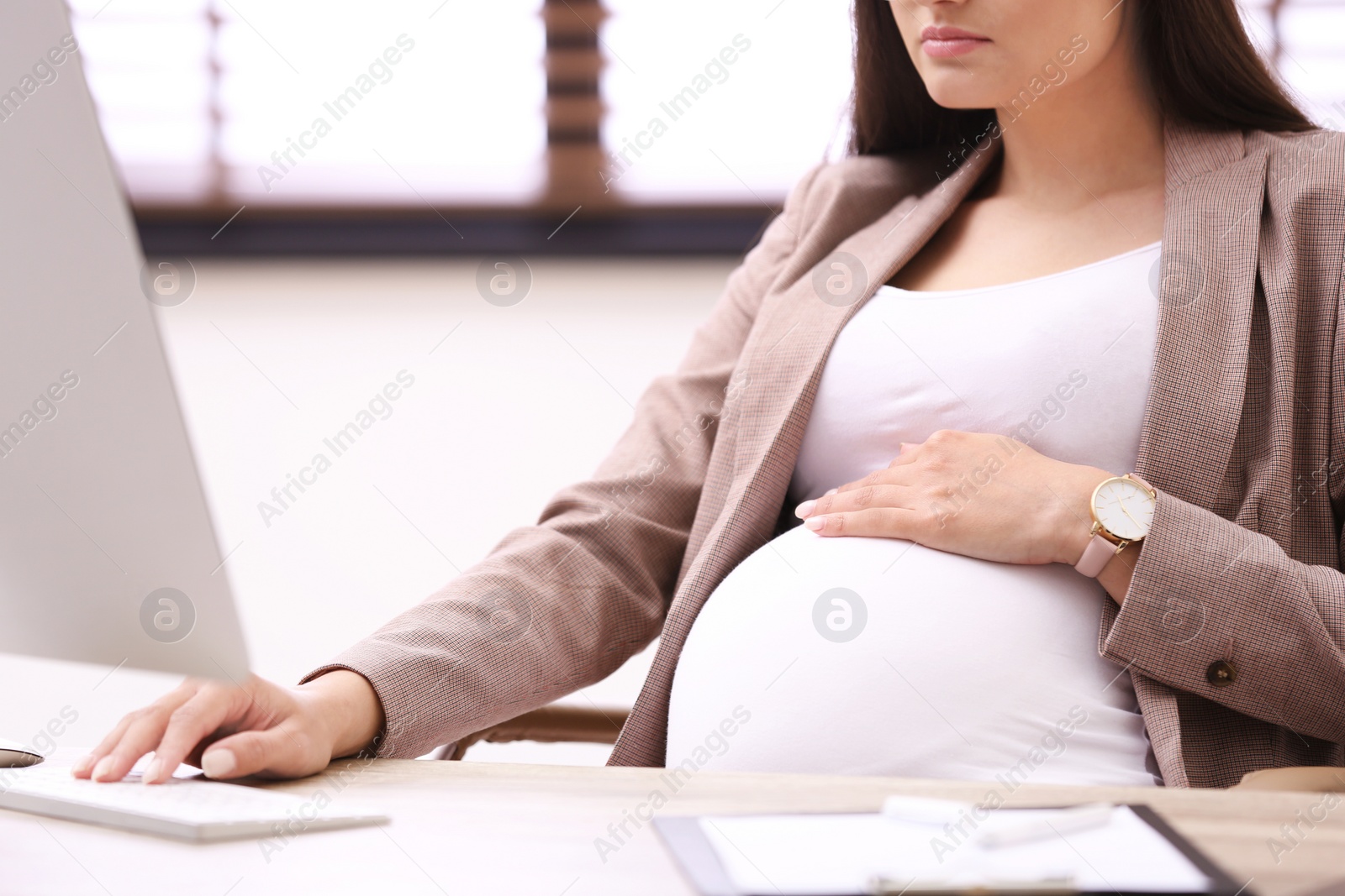 Photo of Young pregnant woman working with computer at table in office, closeup