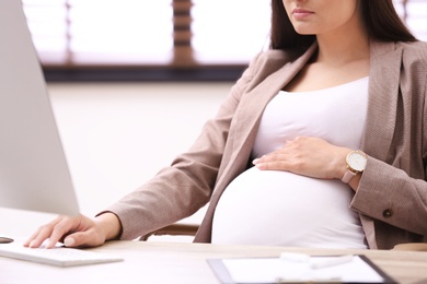 Young pregnant woman working with computer at table in office, closeup