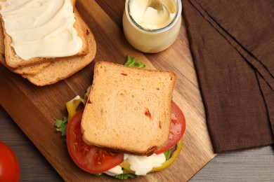 Photo of Delicious sandwich with vegetables and mayonnaise served on wooden table, flat lay