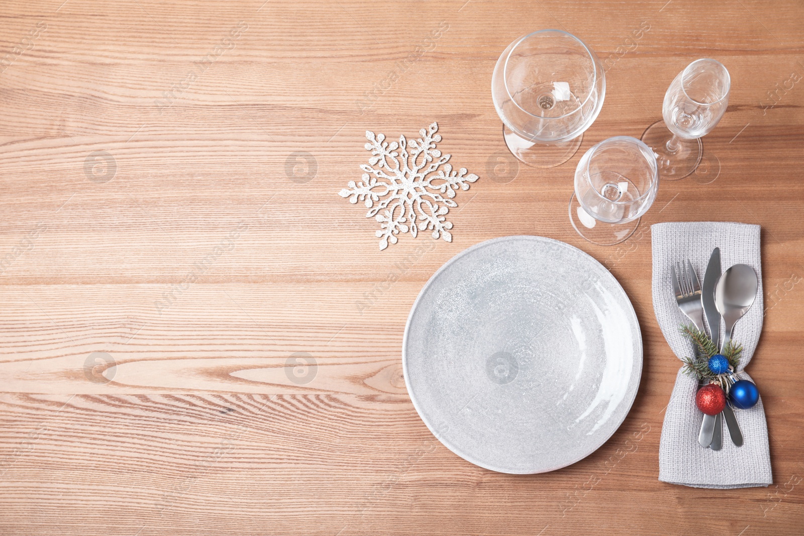 Photo of Christmas table setting with plate, glasses, cutlery and napkin on wooden background, flat lay. Space for text