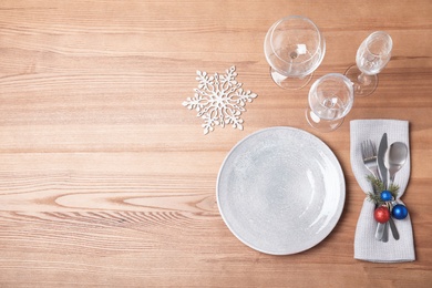 Photo of Christmas table setting with plate, glasses, cutlery and napkin on wooden background, flat lay. Space for text