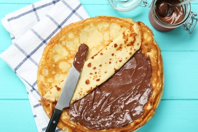 Photo of Tasty crepes with chocolate paste served on turquoise wooden table, flat lay