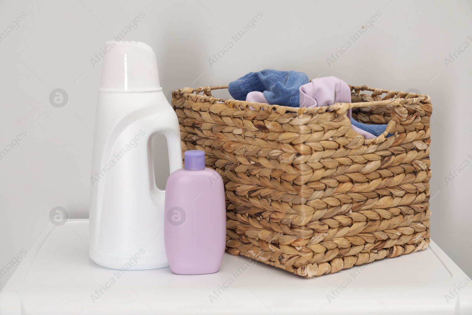 Photo of Baby clothes in wicker basket and laundry detergents on washing machine near light wall