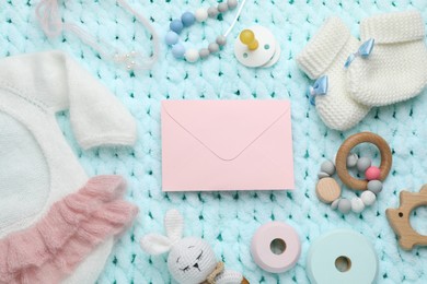 Photo of Baby shower party. Envelope surrounded by stuff for child on light blue knitted fabric, flat lay