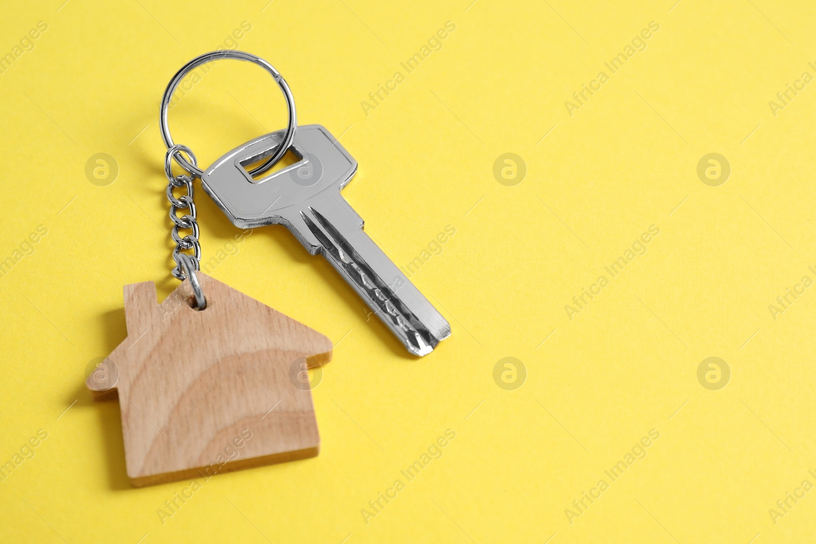 Photo of Key with keychain in shape of house on yellow background, closeup. Space for text