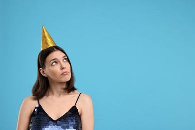 Sad young woman in party hat on light blue background