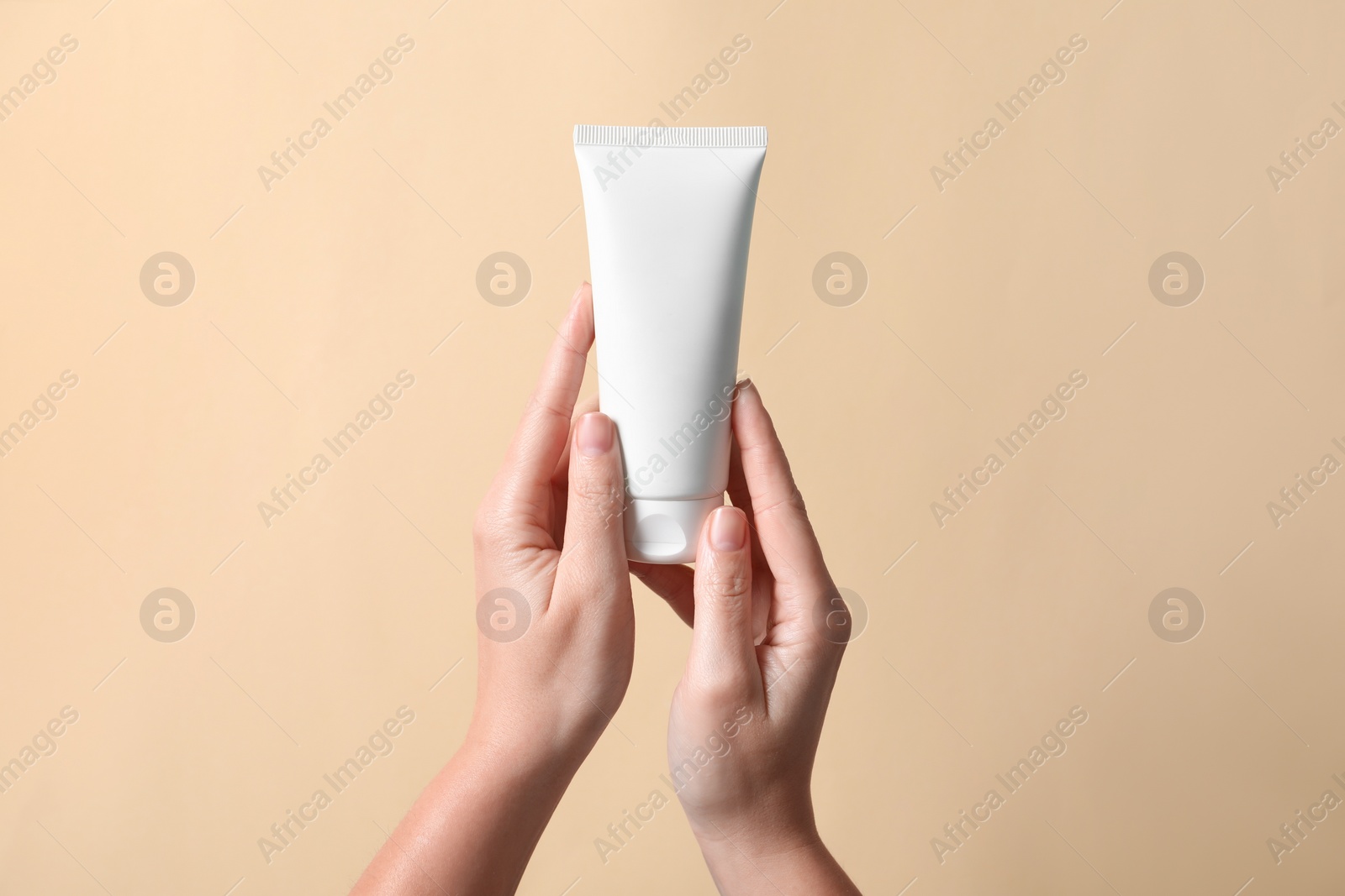 Photo of Woman with tube of hand cream on beige background, closeup