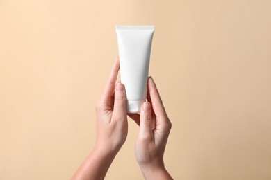Photo of Woman with tube of hand cream on beige background, closeup
