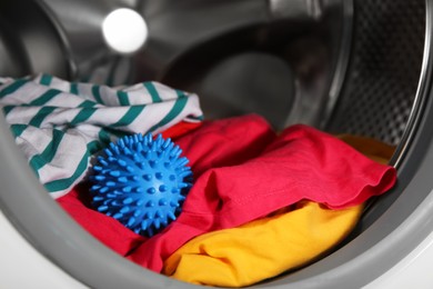 Blue dryer ball and clothes in washing machine drum, closeup