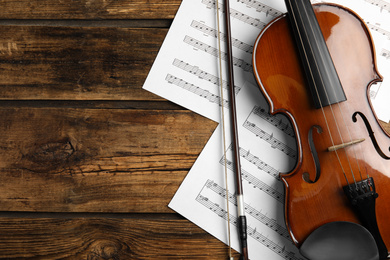 Photo of Beautiful violin, bow and note sheets on wooden table, flat lay. Space for text