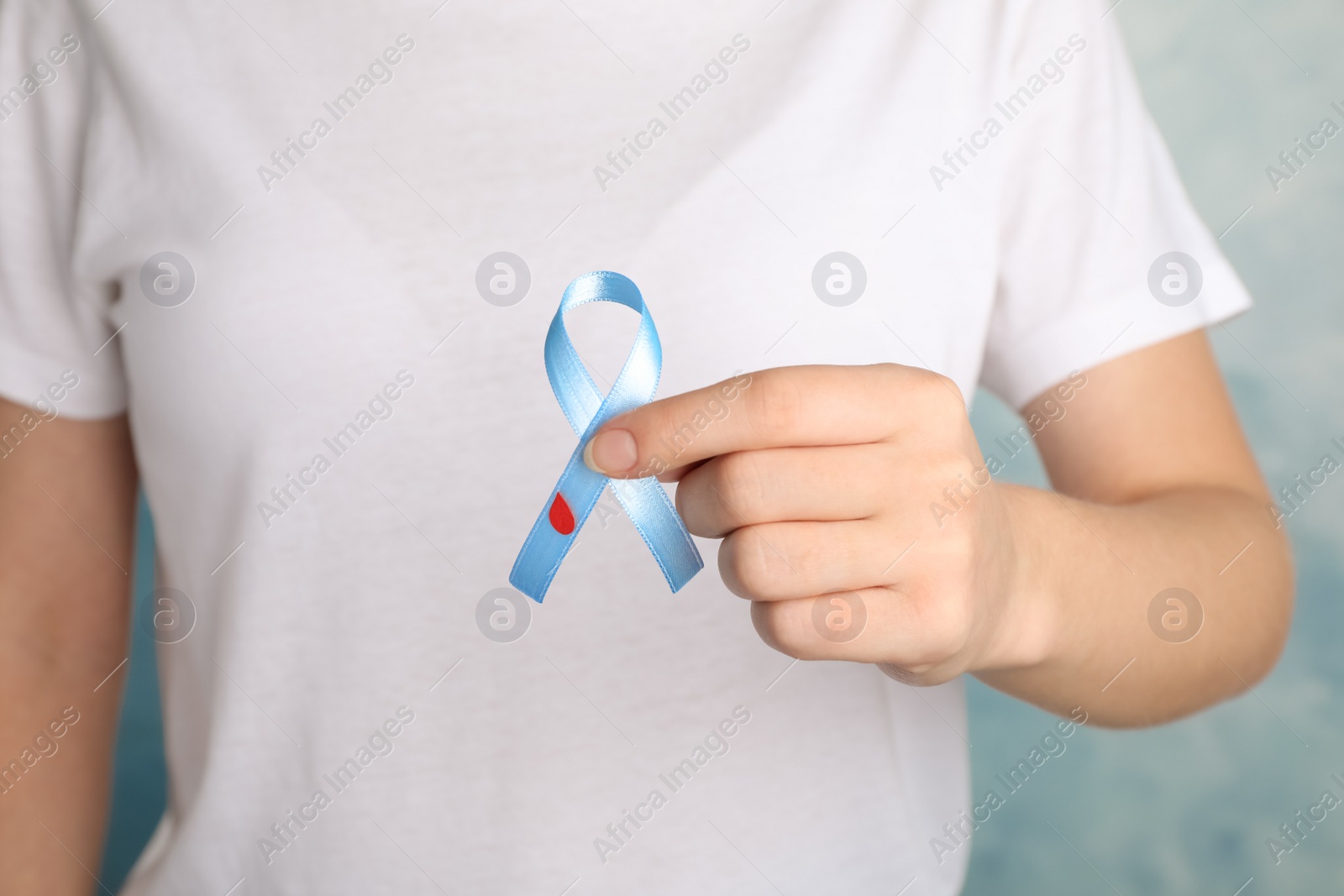 Photo of Woman holding light blue ribbon with paper blood drop on color background, closeup. World Diabetes Day