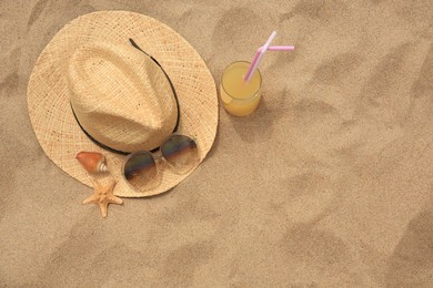 Straw hat, sunglasses, refreshing drink, seashell and starfish on sand, top view with space for text. Beach accessories