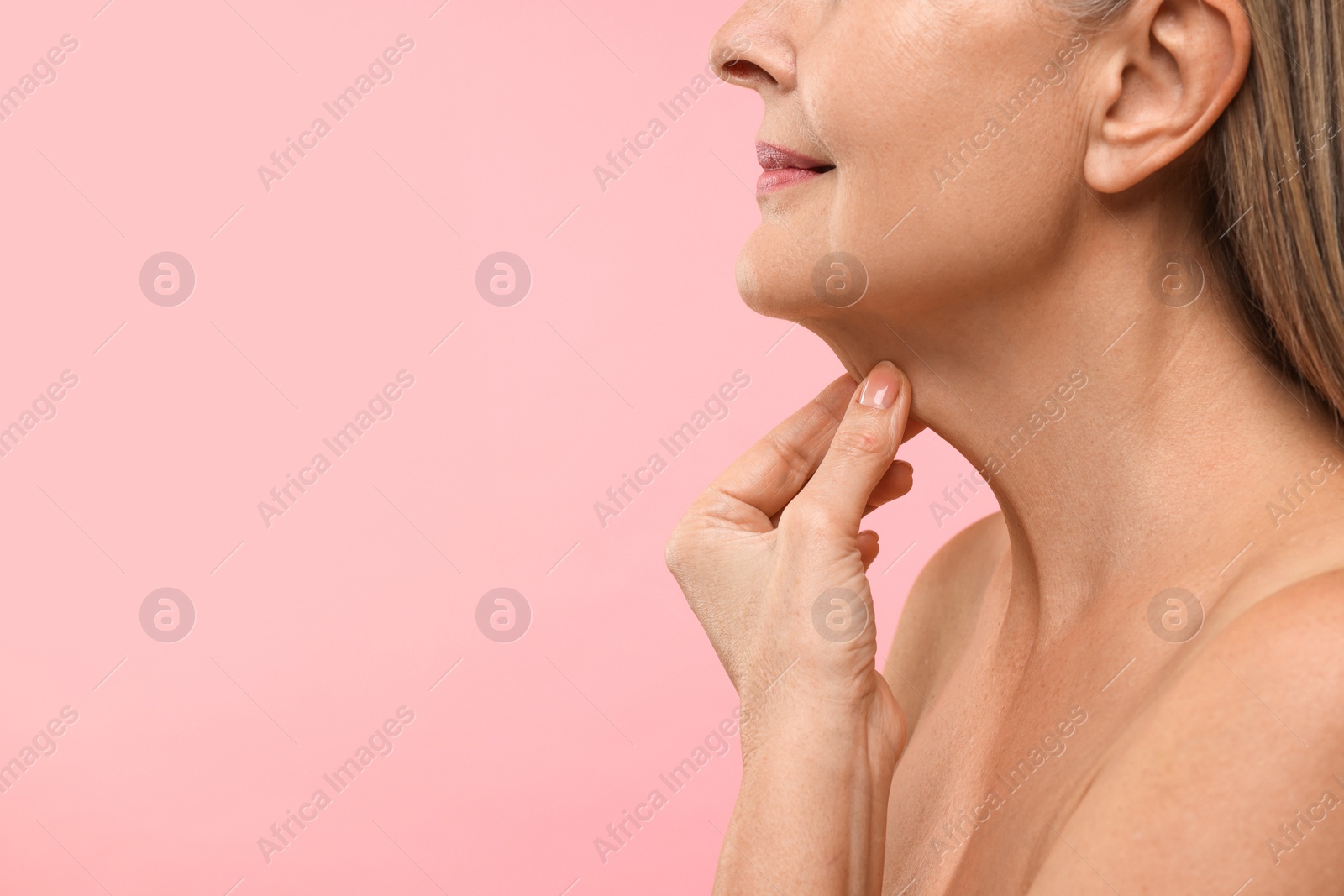 Photo of Mature woman touching her neck on pink background, closeup. Space for text