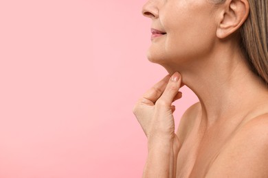 Photo of Mature woman touching her neck on pink background, closeup. Space for text