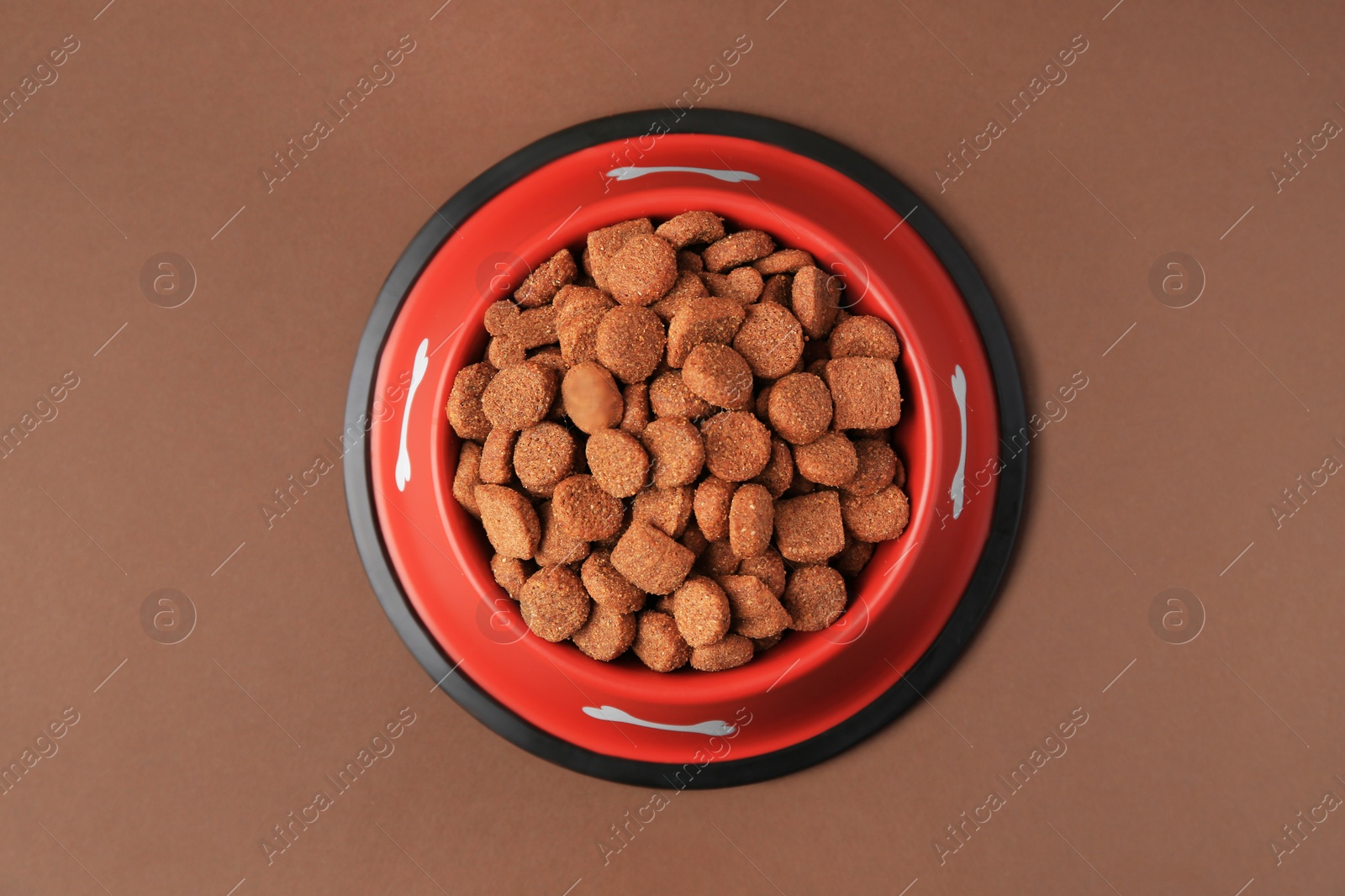 Photo of Dry dog food in feeding bowl on brown background, top view