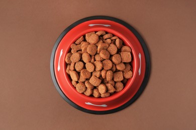 Photo of Dry dog food in feeding bowl on brown background, top view