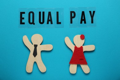 Photo of Equal pay. Wooden figures of man and woman on light blue background, flat lay