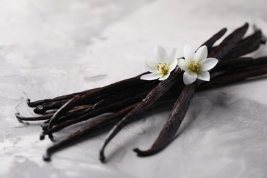 Photo of Vanilla pods and flowers on light textured table, closeup