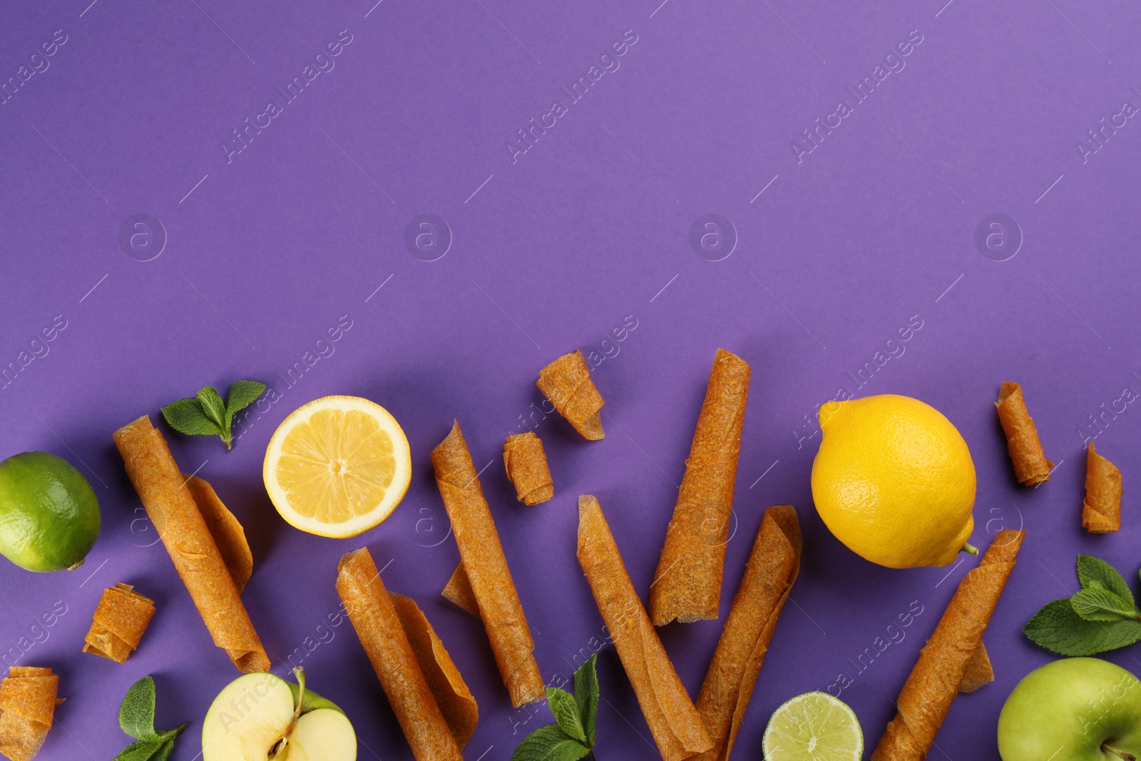 Photo of Flat lay composition with delicious fruit leather rolls on purple background. Space for text