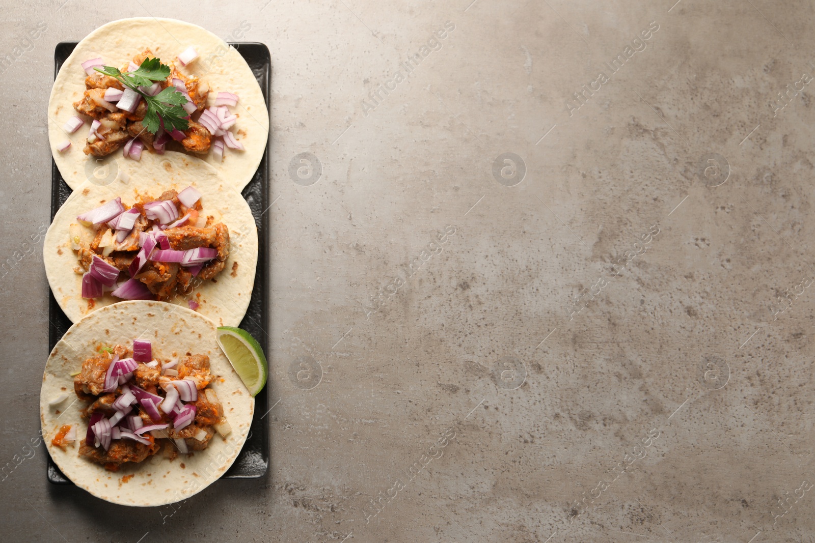 Photo of Delicious tacos with vegetables, meat and lime on grey textured table, top view. Space for text