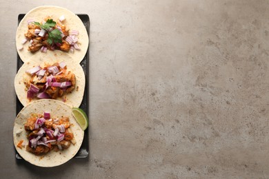 Delicious tacos with vegetables, meat and lime on grey textured table, top view. Space for text