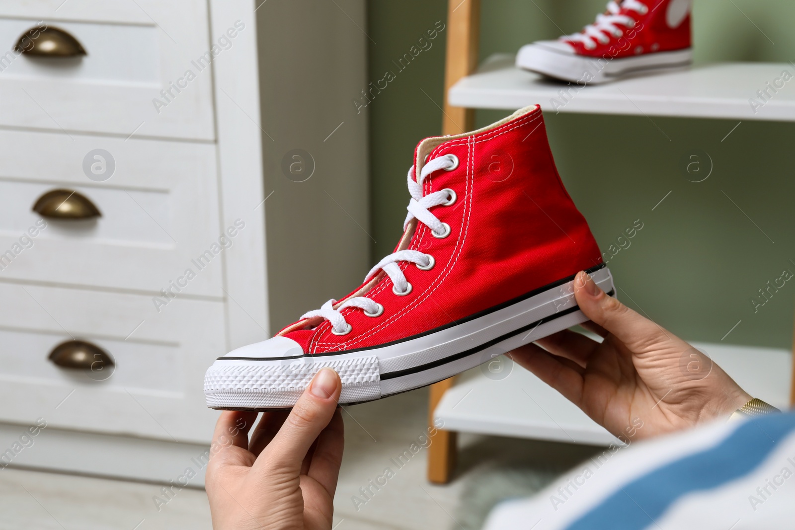 Photo of Woman holding new stylish red sneaker indoors, closeup