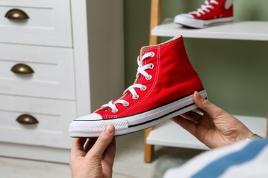 Photo of Woman holding new stylish red sneaker indoors, closeup