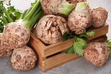 Photo of Fresh raw celery roots and wooden crate on light grey table