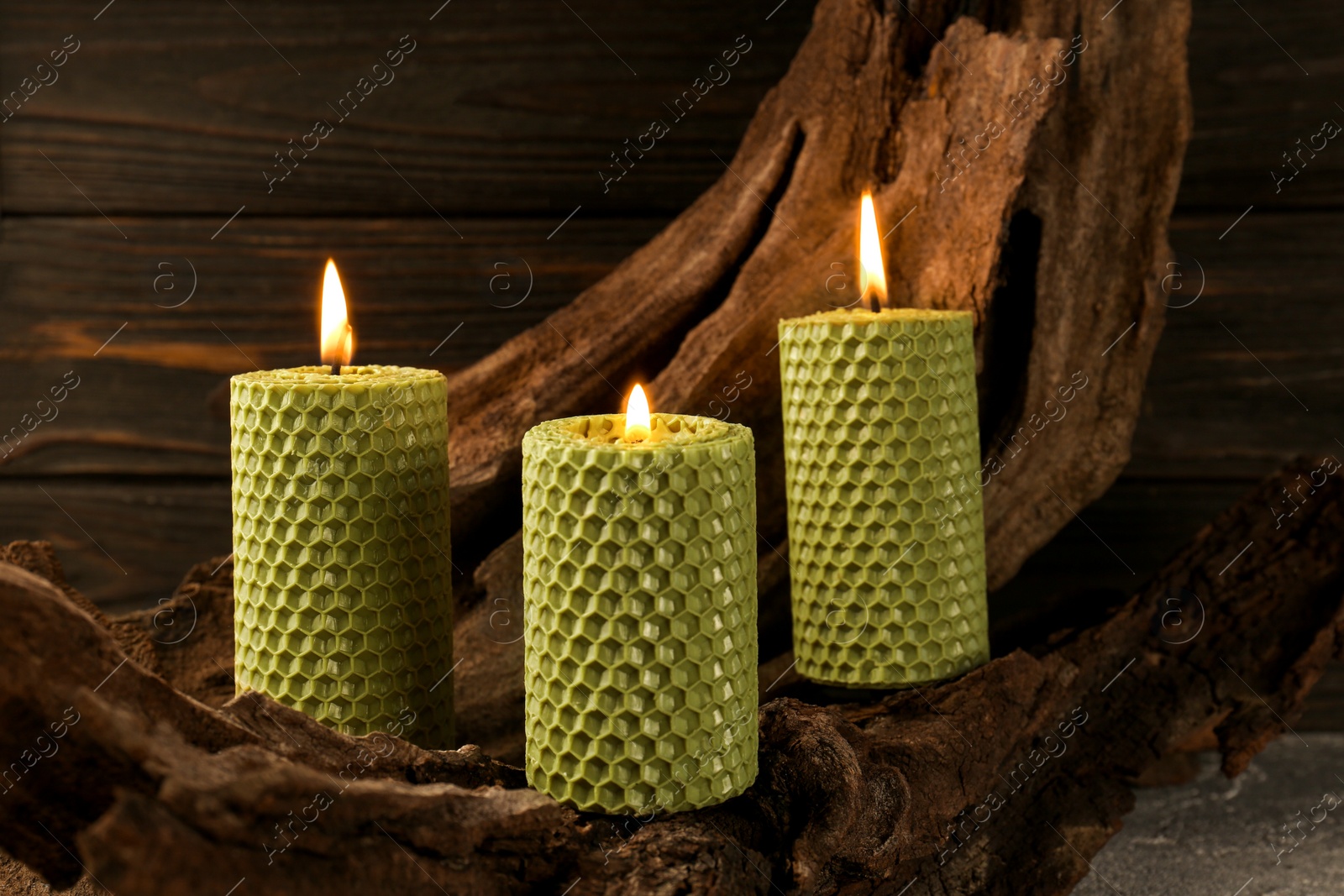 Photo of Beautiful burning beeswax candles on snag near wooden wall