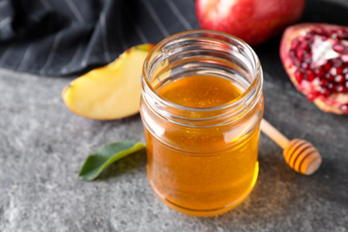 Photo of Honey near pomegranate and apple on grey table, closeup. Rosh Hashanah holiday